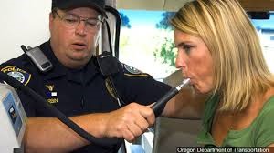 A police officer holding a breathalyzer test as a woman blows into it
